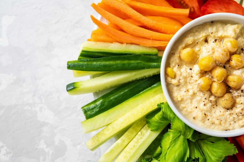 Close up of a plate with raw vegetables and hummus dip