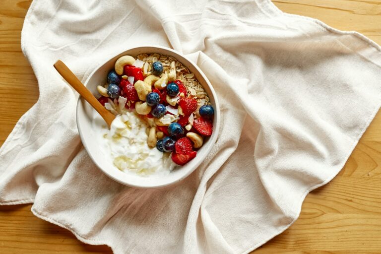 Coconut yogurt granola with strawberry, blueberry and cashew in white bowl.