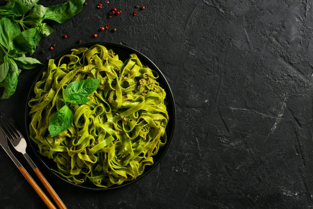 Green vegetarian basil pasta with pesto on black background